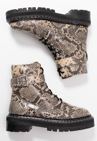 Bottines à motif peau de serpent marron et beige avec une finition texturée, des ferrures argentées, des lacets et une semelle noire épaisse.