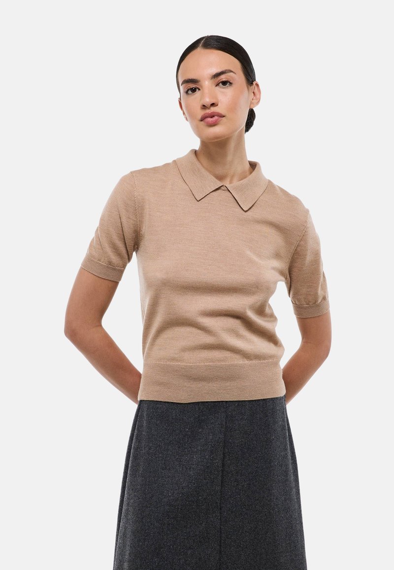 Polo beige à manches courtes avec un col, texture côtelée et taille cintrée, associé à une jupe noire taille haute.
