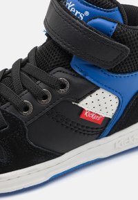 Zapatilla alta negra y azul con una correa de velcro, paneles de malla, acentos perforados en blanco y una etiqueta con el logo rojo en el lateral.