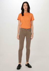 Oranje katoenen T-shirt met korte mouwen, gecombineerd met bruin aangesloten broek en zwarte instappers. Eenvoudig ontwerp met een ronde hals. Soepele textuur.