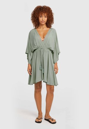 Grünes Wickelkleid mit kurzen Ärmeln, tailliertem Schnitt und Quastenverzierung. Hergestellt aus leichtem Stoff mit weicher Textur und lockerem Sitz.