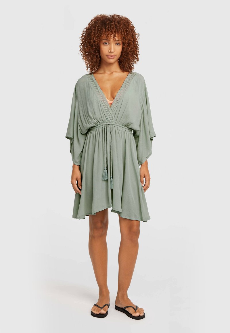Πράσινο φόρεμα με ζώνη, κοντά μανίκια και διακοσμητικά φουντάκια. Κατασκευασμένο από ελαφρύ ύφασμα με απαλή υφή και άνετη εφαρμογή.