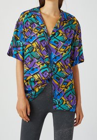 Camisa de manga corta con un patrón abstracto vibrante que presenta colores púrpura, azul, verde y amarillo sobre un fondo negro; corte holgado; tejido ligero.