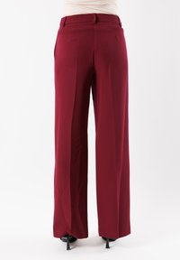 Pantaloni a gamba larga in tessuto borgogna scuro, con pieghe frontali, tasche posteriori e vita con cintura. Texture liscia con una vestibilità sartoriale.