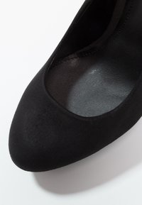 Chaussure à talon haut en suède noir avec un bout arrondi et une doublure intérieure lisse. Présente un design sans couture avec aucune pièce métallique visible.