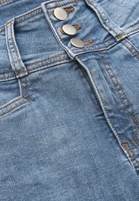 Vaaleansiniset farkut, joissa on korkea vyötärö, kolme hopeista nappia ja oranssia tikkausta saumoissa ja taskuissa.