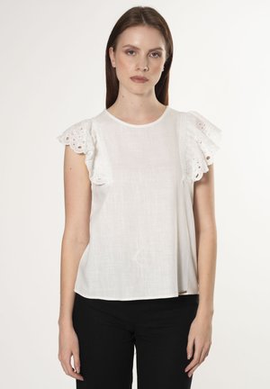 Witte blouse met gerimpelde, oogjeskant mouwen, ronde halslijn en zacht, gestructureerd stof. Gekocht met zwarte broek. Eenvoudige achtergrond.