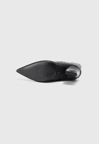 Black high-heeled shoe with a pointed toe, smooth texture, and decorative chain accent along the side, featuring a solid black sole.