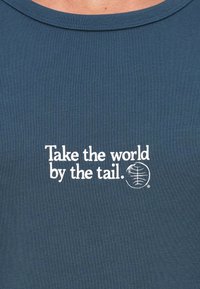 Camisa azul com texto branco "Agarra o mundo pela cauda." e um pequeno logótipo circular com um design estilizado de cauda de lagarto.
