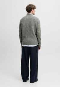 Grauer Strickpullover mit lockerer Passform, runder Halslinie und langen Ärmeln. Über einem weiß gestreiften Hemd getragen und kombiniert mit schwarzen Hosen.