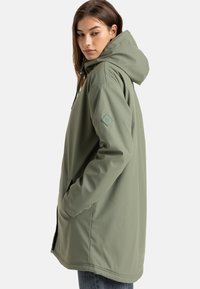 Lichtgroene waterdichte jas met een capuchon, voorzien van een gestructureerde stof, zijzakken en een logo-opdruk op de mouw.