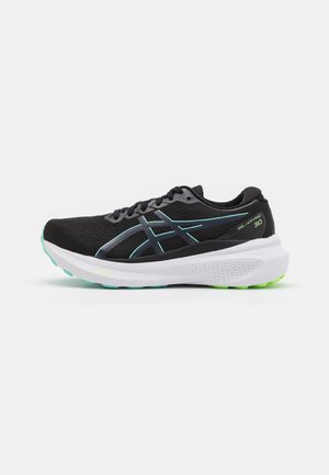 Zapatilla de running negra con detalles en verde azulado, suela blanca y gruesa, bandas con marca y texto "GEL-KAYANO 30" en el lado del talón.