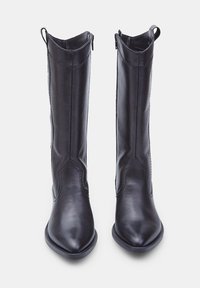 Botas de piel negra hasta la rodilla con puntera afilada, textura suave y detalles de costura en el caña. Incluyen tiras para facilitar su uso.