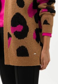 Brun mönstrad cardigan med rosa och svarta leopardfläckar, som har en avslappnad passform och ribbade manschetter, och parats med en rosa topp under.