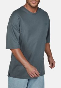 Grijze katoenen t-shirt met korte mouwen, ronde hals, zijsplitten en een klein logo op de borst. Getextureerd, ontspannen pasvorm ontwerp.