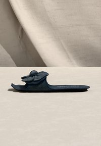 Enkel mørkeblå dames slide-sandal med en stor stoffblomst på den brede øvre stroppen, vist på en lys nøytral overflate.