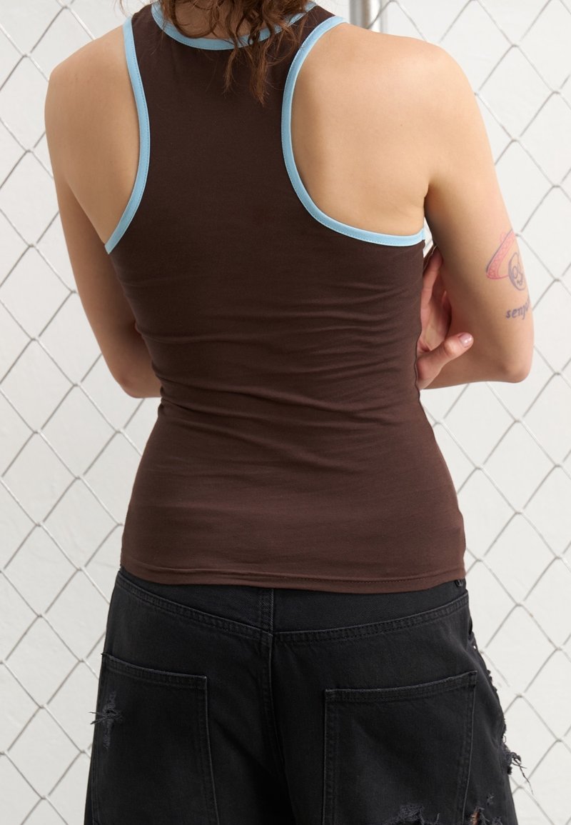 Brun linne med ljusblå kant, åtsittande design och mjuk textur. Bärs med svarta cargoshorts med en slitna finish.