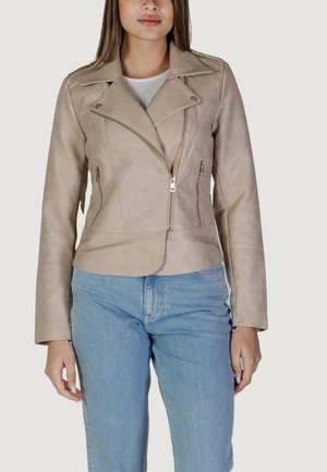 Giacca da moto in ecopelle beige con design aderente, tasche con cerniera e ampi revers, abbinata a jeans in denim azzurro chiaro.