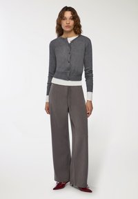 Szary sweter z dzianiny z okrągłym dekoltem i zapięciem na guziki, w połączeniu z szerokimi, teksturowanymi szarymi spodniami oraz czerwonymi butami na obcasie.