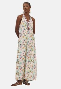 Vestido maxi con cuello halter, patrón floral multicolor sobre un fondo claro, con un detalle en forma de ojal y sandalias planas.