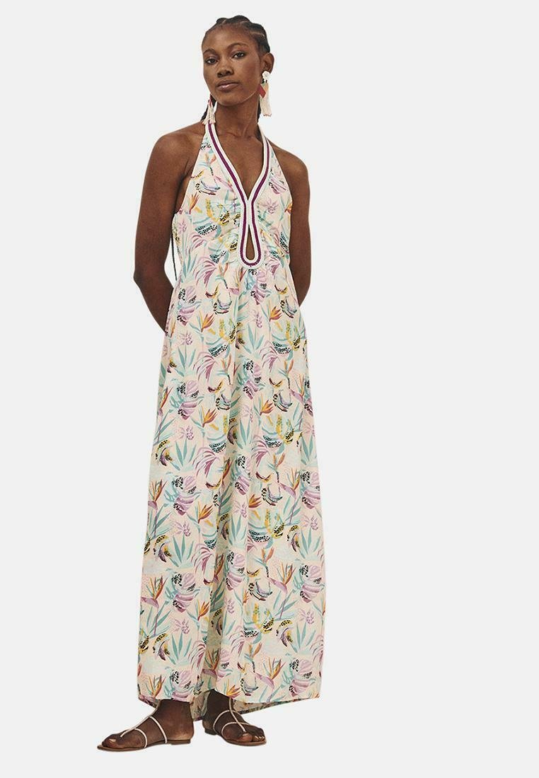 Vestido maxi con cuello halter, patrón floral multicolor sobre un fondo claro, con un detalle en forma de ojal y sandalias planas.