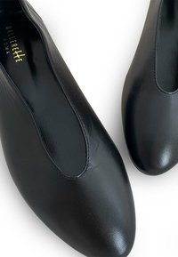 Bailarinas negras de cuero con textura suave, punta redonda y paneles elásticos en los laterales. Logo dorado visible en la plantilla.