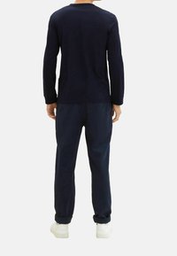 Marinblå långärmad topp med rundad halsringning, kombinerad med matchande marinblå byxor, som har en avslappnad passform och mjuk textur. Vita sneakers kompletterar outfiten.