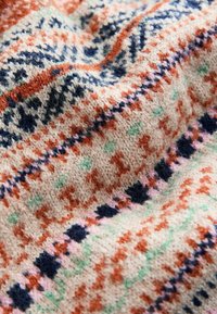 Megztas tekstilė, turinti kreminę bazę su daugybe geometrinių raštų oranžinės, tamsiai mėlynos, rožinės ir žalios spalvų, demonstruojanti švelnų, tekstūruotą paviršių.
