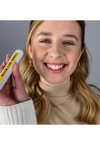 Lekki, biały produkt kosmetyczny z żółtym napisem „(Curl Bounce)” trzymany w dłoni, charakteryzujący się gładką powierzchnią na neutralnym tle.