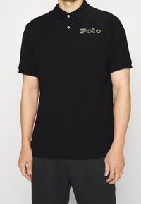 Black cotton polo shirt with a classic collar, two buttons, and "Polo" embroidered in gold on the left chest. Short sleeves, smooth texture.