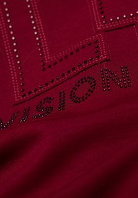 Weinroter Stoff mit erhabenen schwarzen Strasssteinen, die "VISION" buchstabieren, und geometrischen Mustern. Glatte Textur mit dezentem Glanz.