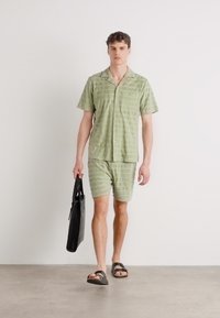 Light green short-sleeve shirt and matching shorts with a textured pattern, paired with a black bag and sandals. Simple design and relaxed fit.