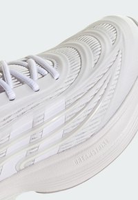 Chaussure de sport blanche avec tissu texturé, empiècements synthétiques incurvés et semelle extérieure amortissante avec détail embossé "DREAM STRIKE".