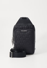 Black sling bag made of textured synthetic material, featuring a geometric pattern and silver hardware. Includes an adjustable strap.