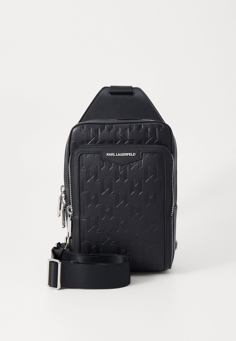 Black sling bag made of textured synthetic material, featuring a geometric pattern and silver hardware. Includes an adjustable strap.