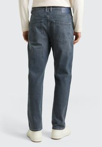 Blauwe denim jeans met een rechte pasvorm, voorzien van twee achterzakken met gebogen stiksels en een effen tailleband. Gedragen met witte sneakers.
