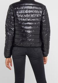 Black puffer jacket with a shiny, quilted texture, featuring horizontal stitching and a fitted design, extending to the waist.
