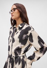 Μαύρο και κρεμ φορεματάκι με σχέδιο, μακριά μανίκια, γιακά, κουμπάκια μπροστά και ζώνη στη μέση. Κατασκευασμένο από υφή υφάσματος.