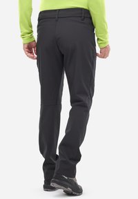 Pantalon softshell noir à coupe slim, doté d'une poche arrière et de genoux articulés, associé à des chaussures sombres. Le matériau semble léger et extensible.