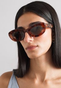 Lunettes de soleil en acétate écaille de tortue en forme d'yeux de chat avec des verres foncés, des montures lisses et des branches larges, affichant un design inspiré du rétro.