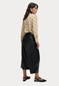 Beige blus med svarta prickar, knäppta ärmar; svarta fusk läder culotter; svarta platta skor med spännen.