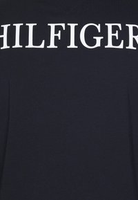 Marineblaues Baumwoll-T-Shirt mit V-Ausschnitt und großem weißen "HILFIGER"-Text auf der Brust. Glatte Textur ohne Muster oder Akzente.