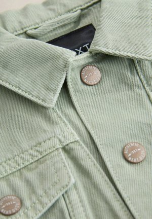 Hellgrünes Denimhemd mit spitzem Kragen, Knopfverschluss und dekorativer bronzefarbener Hardware mit Gravur "Authentic 1982".