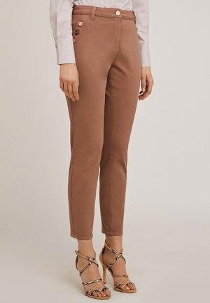 Pantalones marrones ajustados con una textura suave, que presentan un detalle de botón en el costado y se combinan con sandalias de tacón alto con tiras.