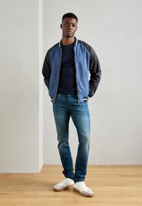 Chaqueta bomber azul con mangas negras, camiseta navy, jeans azules y zapatillas blancas. Look casual con cremallera y detalles de canalé.