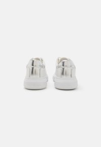 White sneakers with a shiny metallic silver back, smooth leather upper, round toe, and a textured rubber sole. Brand name embossed at heel.
