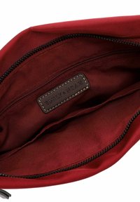 Interno di una borsa di tessuto rosso con una superficie liscia, dotata di una zip nera e di un'etichetta in pelle con la scritta "EMILY & NOAH" impressa.