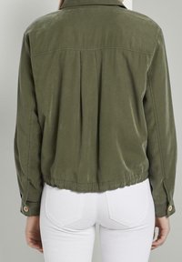 Giacca leggera verde oliva con schiena plissettata, orlo elastico e polsini con bottoni. Realizzata in tessuto morbido con una vestibilità sartoriale.