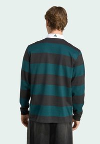 Chemise à manches longues noire et à rayures turquoise, avec un col blanc et des textures contrastées, et un détail de logo à l'arrière du col.