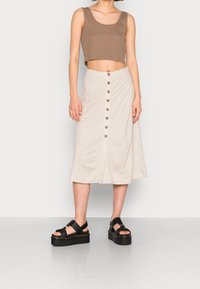 Top corto marrón, falda midi beige con botones y sandalias negras de plataforma con tiras. Textura suave y diseño sencillo.